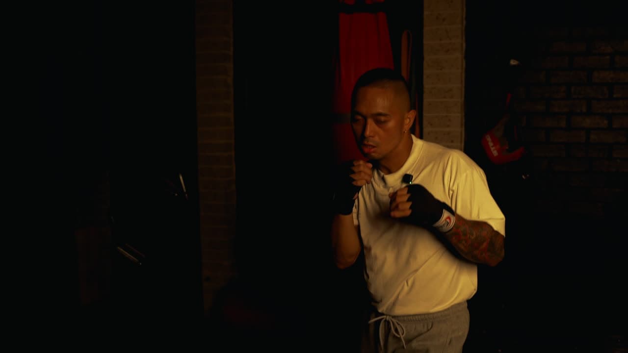 A boxer holding a tight guard against the wall in a dark, dramatically lit gym.