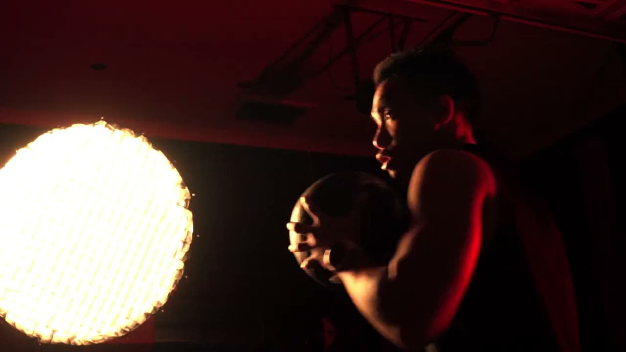 An athlete gripping a medicine ball under dramatic red gym lighting.