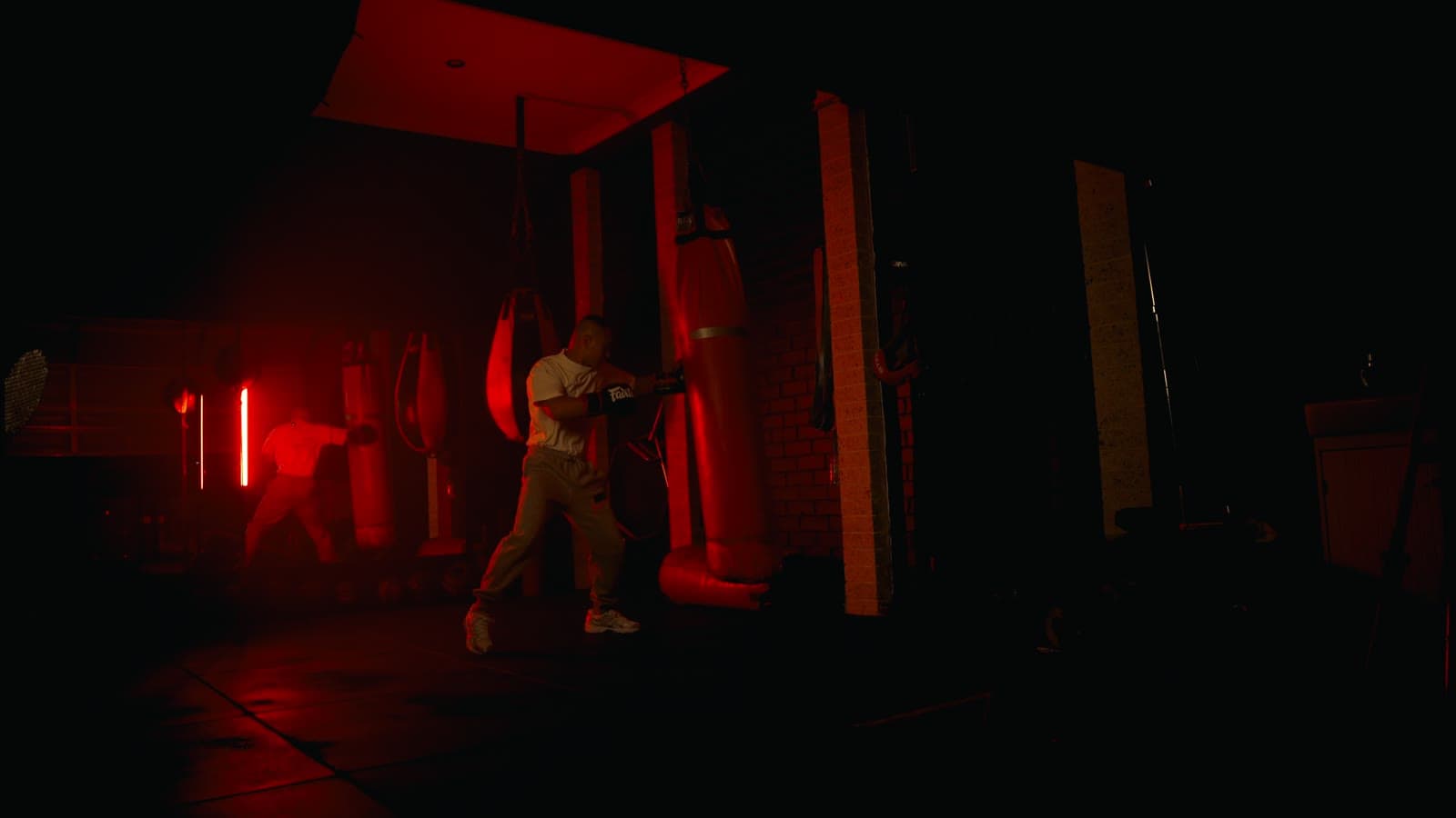 A boxer driving combinations into a heavy bag in a dark, red-lit gym.